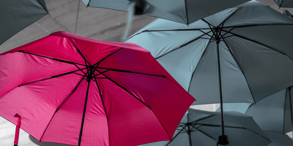 Flera gråa paraplyn och ett rosa paraply